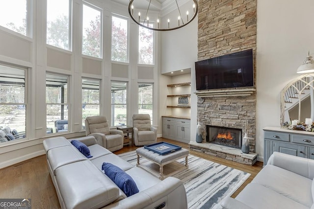 living room featuring a stone fireplace, a high ceiling, hardwood / wood-style flooring, a notable chandelier, and crown molding