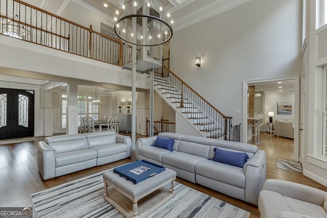 living room featuring crown molding, wood-type flooring, a towering ceiling, and a notable chandelier