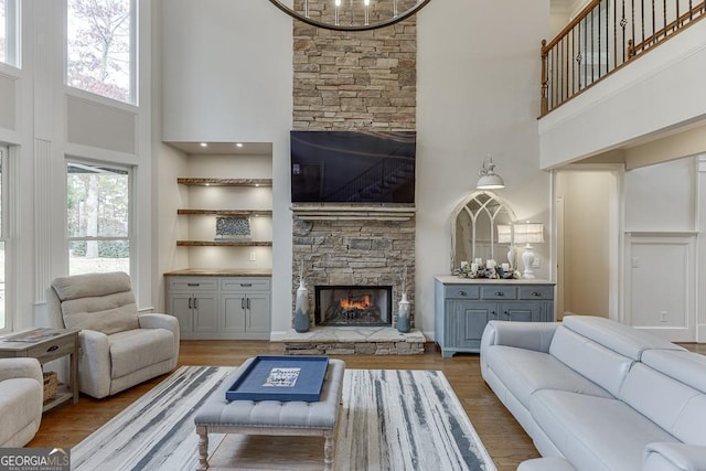 living room featuring a stone fireplace, wood-type flooring, and a high ceiling