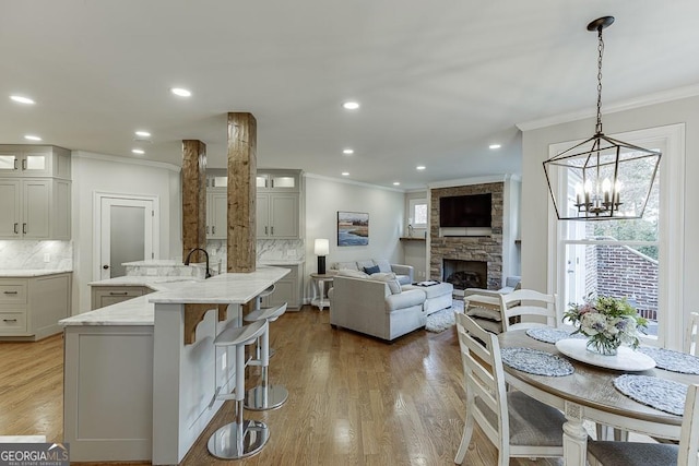 kitchen featuring a stone fireplace, tasteful backsplash, light stone counters, a center island with sink, and pendant lighting