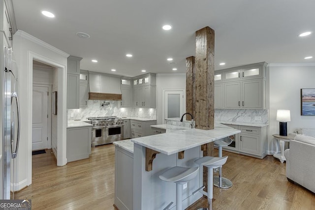 kitchen with backsplash, a kitchen bar, custom exhaust hood, light stone counters, and stainless steel appliances