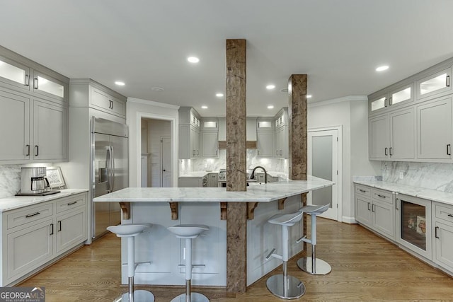 kitchen with a breakfast bar area, stainless steel built in refrigerator, tasteful backsplash, light stone counters, and an island with sink