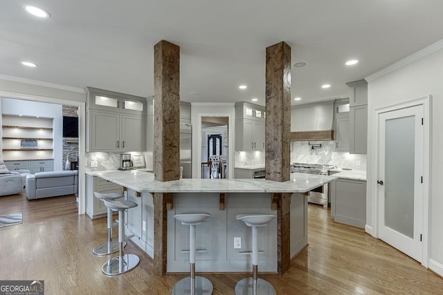 kitchen with premium range hood, a breakfast bar, ornate columns, light stone counters, and high end range