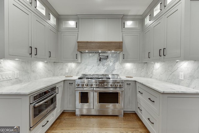 kitchen with light stone countertops, decorative backsplash, stainless steel appliances, and premium range hood