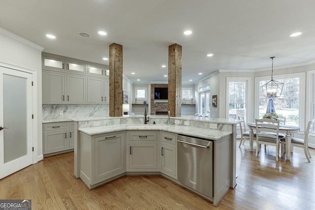 kitchen featuring hanging light fixtures, light wood-type flooring, stainless steel dishwasher, an island with sink, and light stone countertops