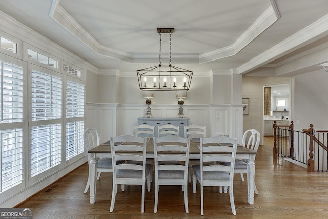 dining area featuring hardwood / wood-style flooring, ornamental molding, an inviting chandelier, and a tray ceiling