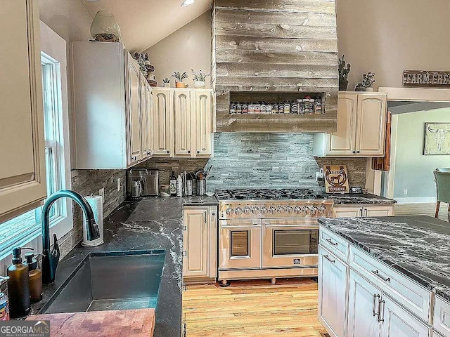 kitchen with sink, vaulted ceiling, light hardwood / wood-style flooring, decorative backsplash, and range with two ovens