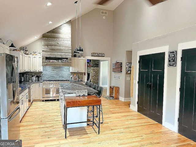 kitchen featuring a kitchen island, appliances with stainless steel finishes, a breakfast bar, high vaulted ceiling, and tasteful backsplash