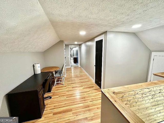 corridor with lofted ceiling, light wood-type flooring, and a textured ceiling