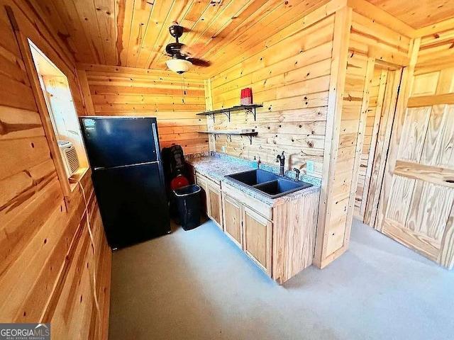 kitchen featuring light brown cabinetry, sink, wood ceiling, black refrigerator, and wooden walls