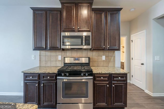 kitchen with appliances with stainless steel finishes, dark brown cabinets, dark hardwood / wood-style floors, light stone counters, and decorative backsplash