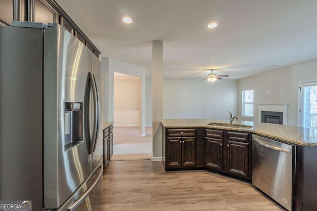 kitchen with appliances with stainless steel finishes, sink, light hardwood / wood-style floors, light stone countertops, and dark brown cabinets