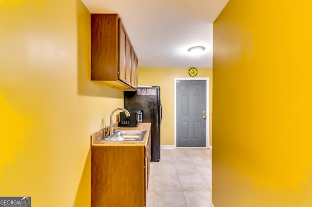 kitchen featuring light tile patterned flooring, sink, and black refrigerator