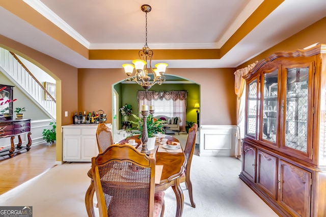 carpeted dining space with a chandelier, ornamental molding, and a raised ceiling