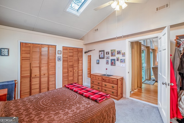 carpeted bedroom featuring ceiling fan, two closets, high vaulted ceiling, and a skylight