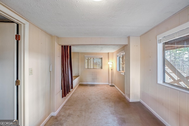 hallway with light colored carpet, wooden walls, and a textured ceiling