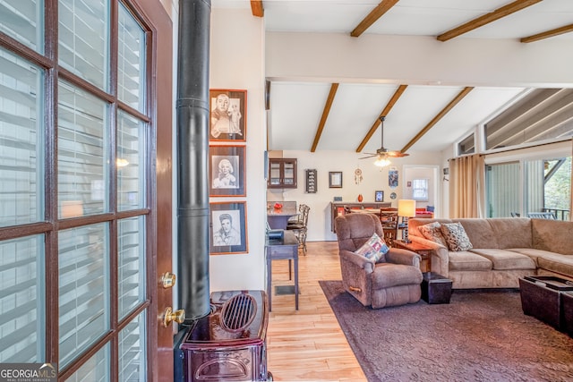 living room featuring hardwood / wood-style flooring, lofted ceiling with beams, ceiling fan, and a wood stove