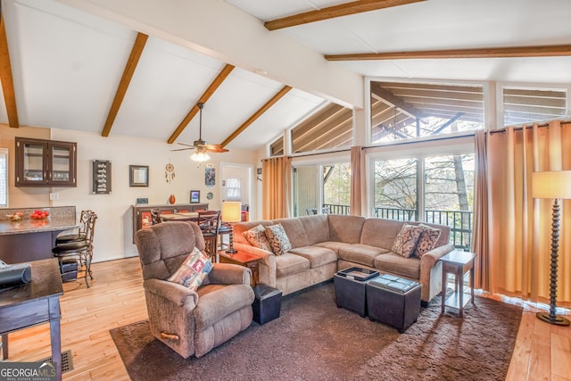 living room featuring ceiling fan, light wood-type flooring, and vaulted ceiling with beams