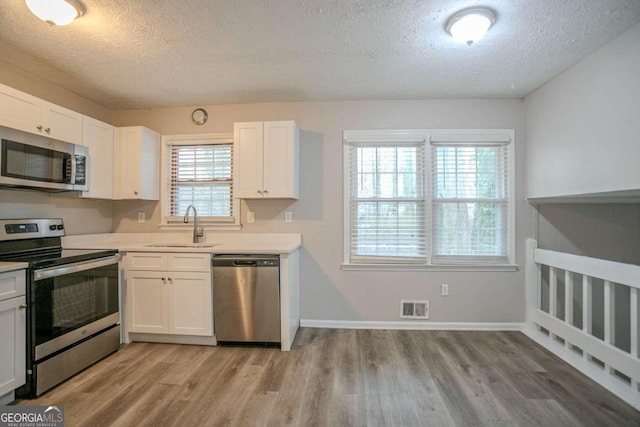 kitchen with white cabinetry, stainless steel appliances, sink, and light wood-type flooring