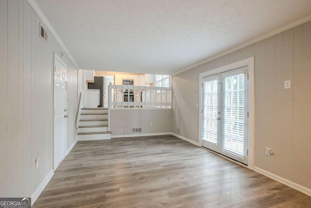 unfurnished living room featuring crown molding, hardwood / wood-style floors, a textured ceiling, and wood walls