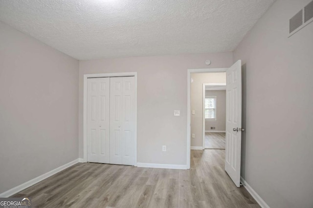 unfurnished bedroom with light hardwood / wood-style floors, a closet, and a textured ceiling