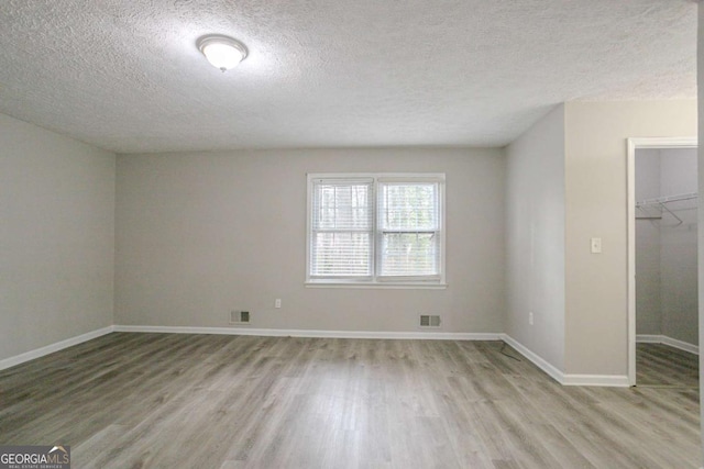 empty room with a textured ceiling and light hardwood / wood-style flooring