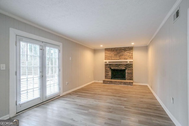 unfurnished living room featuring wood walls, light wood-type flooring, ornamental molding, a brick fireplace, and a textured ceiling