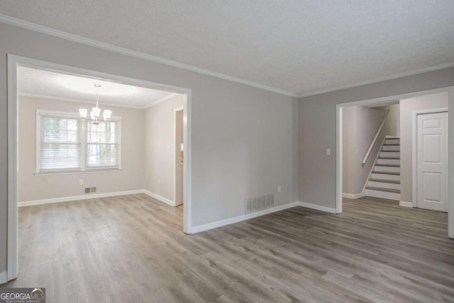 empty room with ornamental molding, hardwood / wood-style floors, a notable chandelier, and a textured ceiling