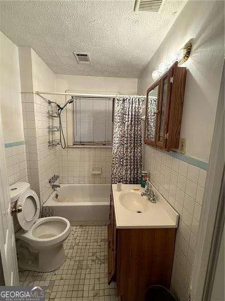 full bathroom featuring shower / bath combo, tile walls, vanity, a textured ceiling, and toilet