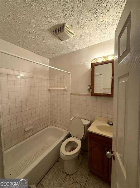 full bathroom with tile walls, vanity, tile patterned floors, toilet, and tiled shower / bath