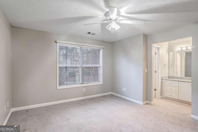 unfurnished bedroom with ceiling fan, light colored carpet, a textured ceiling, and ensuite bath