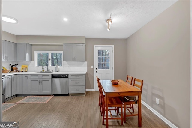 kitchen featuring sink, stainless steel dishwasher, gray cabinets, hardwood / wood-style flooring, and decorative backsplash