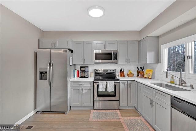 kitchen with sink, light hardwood / wood-style flooring, appliances with stainless steel finishes, gray cabinetry, and tasteful backsplash