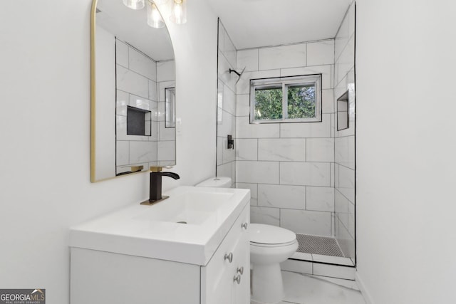 bathroom featuring vanity, a tile shower, and toilet