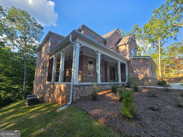 view of home's exterior with covered porch, brick siding, a lawn, and central AC unit