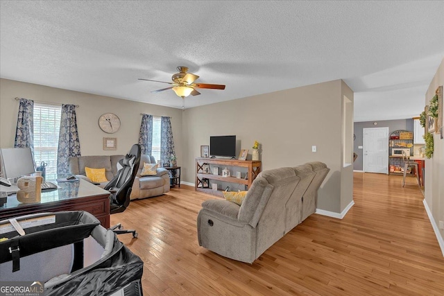 living room with a textured ceiling, ceiling fan, and light hardwood / wood-style flooring