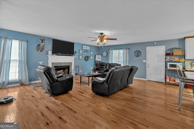 living room with ceiling fan, a textured ceiling, light hardwood / wood-style floors, and a healthy amount of sunlight