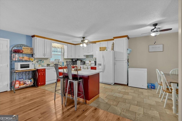 kitchen featuring tasteful backsplash, white cabinetry, a breakfast bar area, a center island, and white appliances