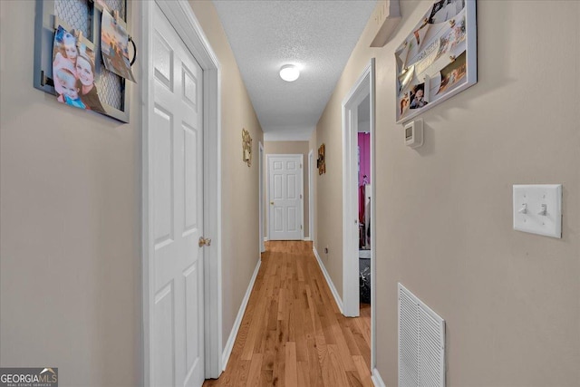 hall featuring light wood-type flooring and a textured ceiling