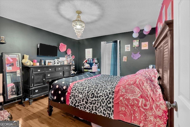 bedroom featuring an inviting chandelier, light hardwood / wood-style flooring, and a textured ceiling