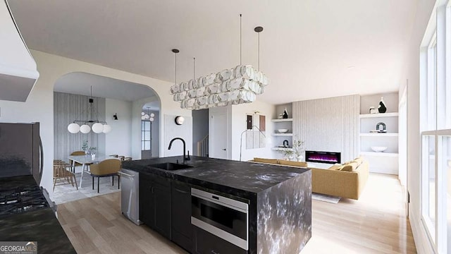 kitchen with appliances with stainless steel finishes, built in features, sink, a center island with sink, and light hardwood / wood-style flooring