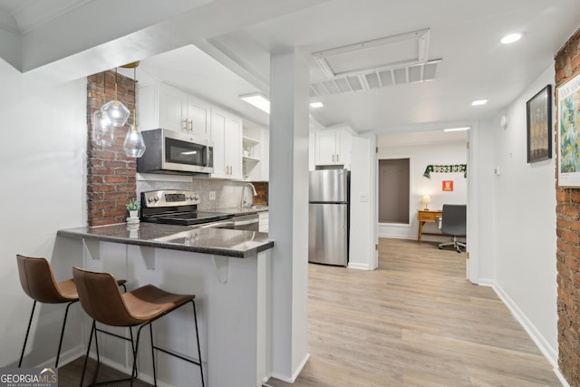 kitchen featuring white cabinetry, dark stone countertops, light hardwood / wood-style floors, kitchen peninsula, and stainless steel appliances