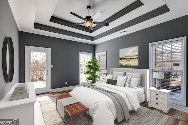 bedroom with access to exterior, ceiling fan, a tray ceiling, crown molding, and light wood-type flooring