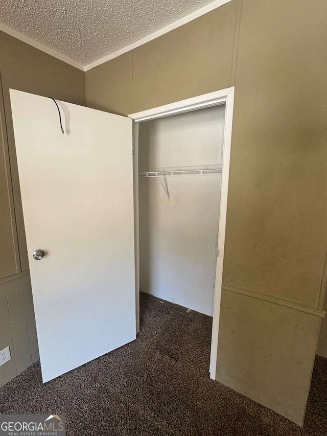 unfurnished bedroom featuring a textured ceiling, dark carpet, and a closet