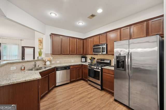 kitchen featuring sink, appliances with stainless steel finishes, light stone counters, light hardwood / wood-style floors, and kitchen peninsula