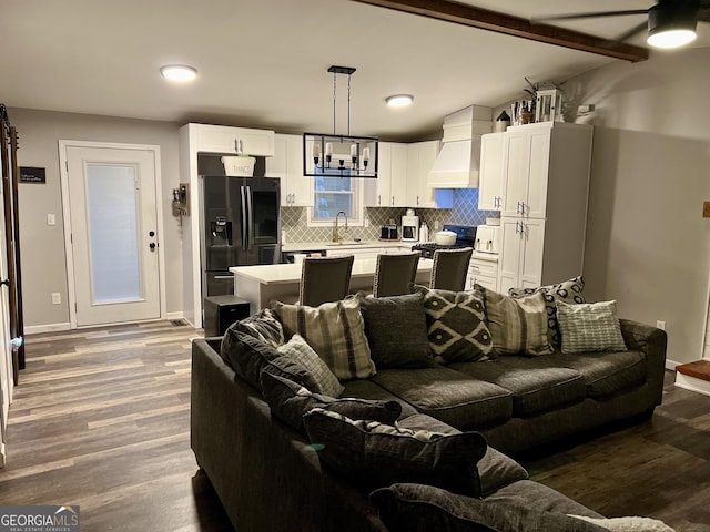 living room featuring lofted ceiling with beams, sink, a notable chandelier, and light hardwood / wood-style floors