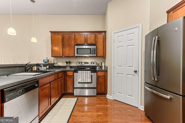 kitchen featuring dark wood-type flooring, appliances with stainless steel finishes, sink, and hanging light fixtures