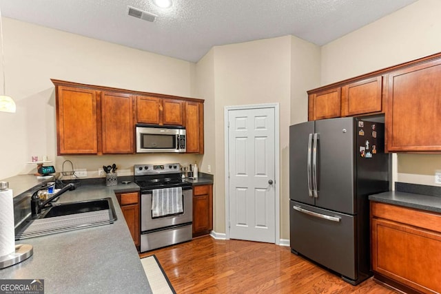 kitchen with appliances with stainless steel finishes, dark hardwood / wood-style flooring, sink, and a textured ceiling