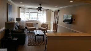 living room featuring crown molding, wood-type flooring, a barn door, and ceiling fan