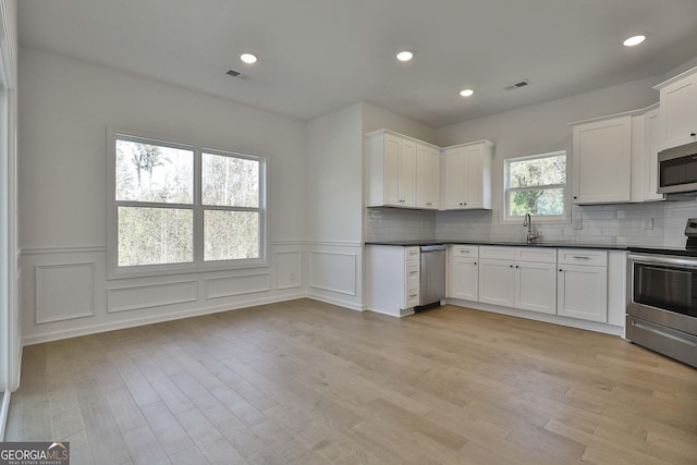 kitchen featuring sink, white cabinetry, tasteful backsplash, appliances with stainless steel finishes, and light hardwood / wood-style floors